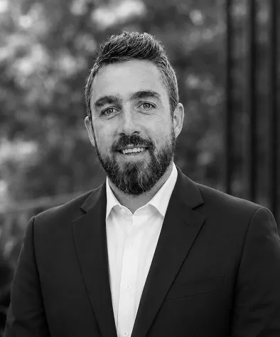 Black and white portrait of a man with a beard, wearing a suit and smiling at the camera.